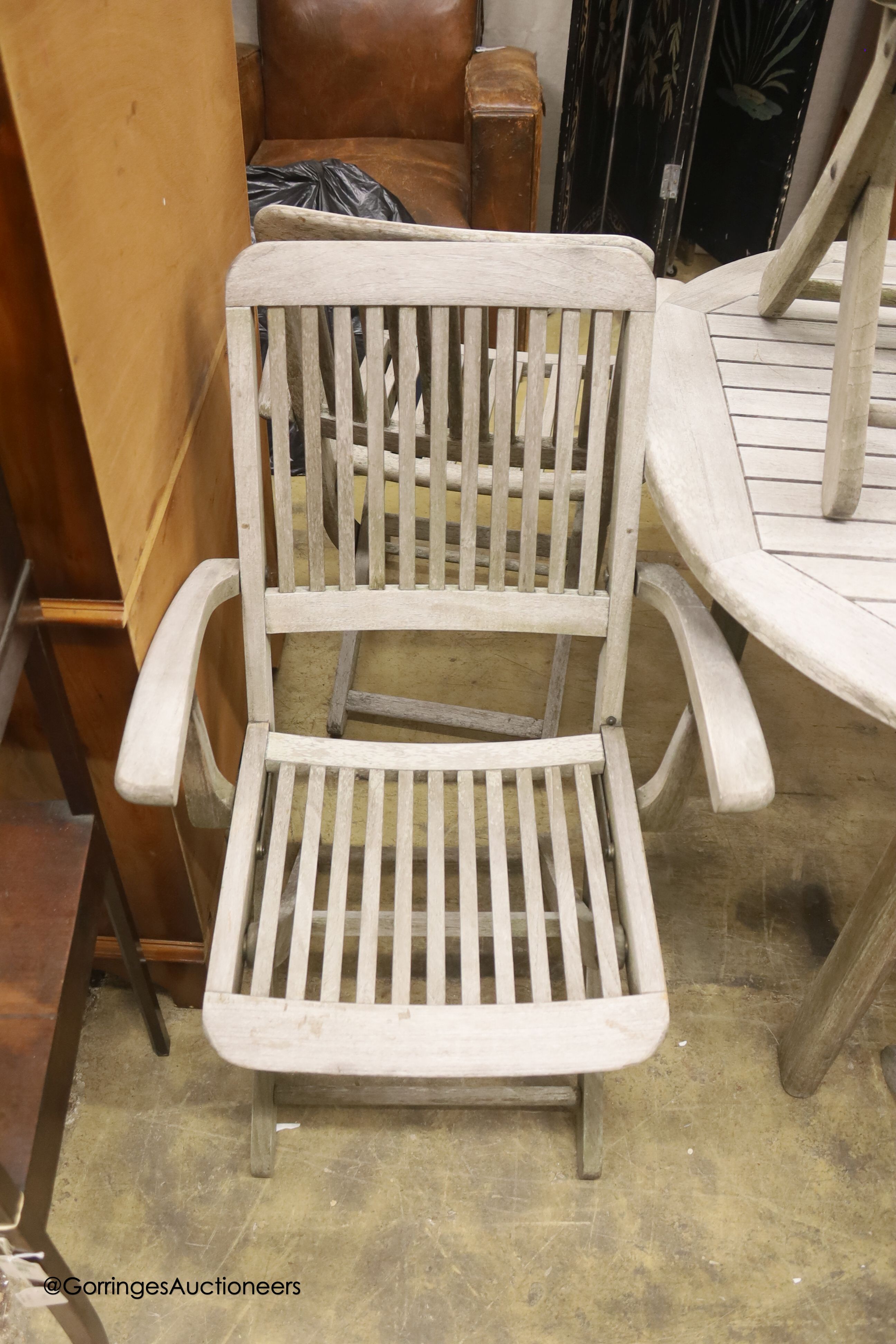 A weathered teak extending garden table, diameter 128cm, height 68cm and six folding elbow chairs